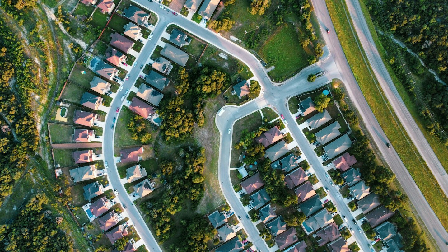 Suburban neighborhood with houses and trees beside a highway.